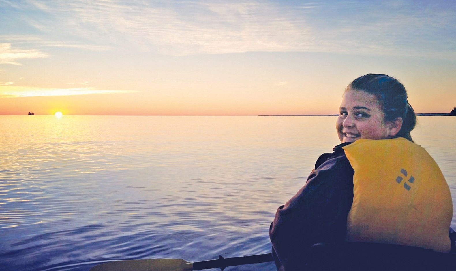 At right: At about 7 a.m., Izzy Nizschke looks back at her father, Kyle Nitzschke, during the kayak trip to Round Island Monday, August 29. In the distance, to the left, a freighter is seen on the horizon shortly after sunrise. (Photograph courtesy Holly Nitzschke)